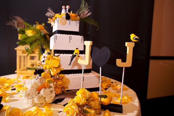 White four tiered square wedding cake with a border of black strips and polka dots accented with yellow, gold, and orange floral decorations and orioles - photo by Orange County based wedding photographers Mark Brooke